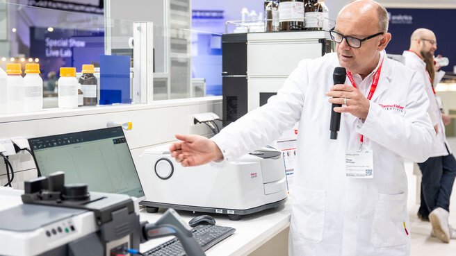 A laboratory expert demonstrates a device with a microphone at the booth