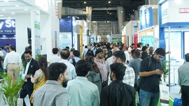 A crowd moving through a bustling trade show or exhibition with booths and displays, making connections.