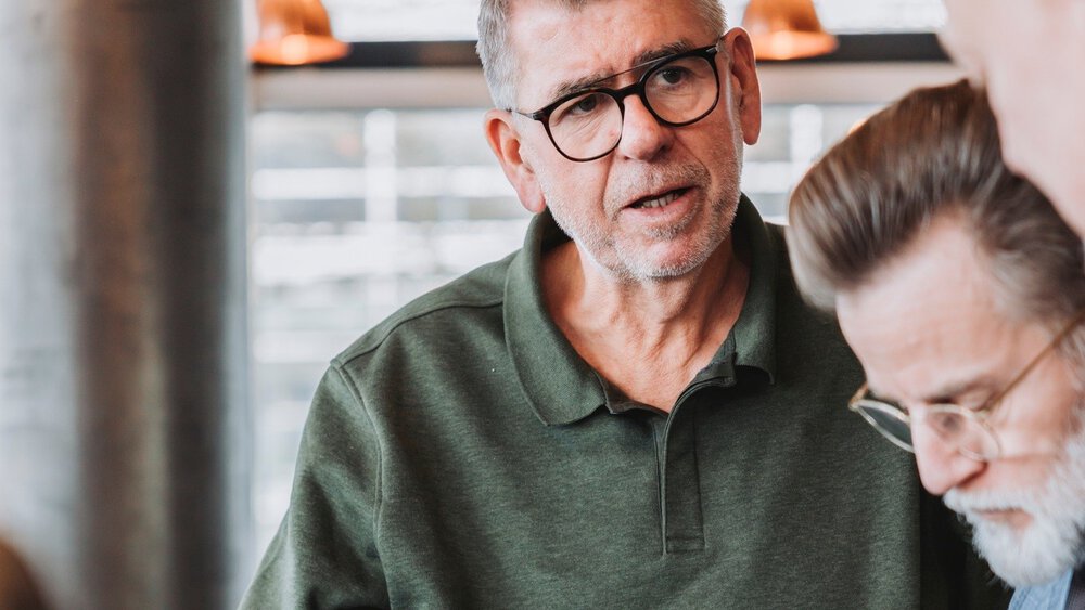 Three men are standing together and discussing a wristwatch that one of the men is holding in his hand.