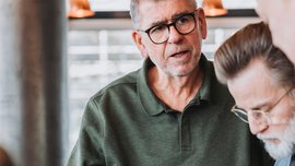 Three men are standing together and discussing a wristwatch that one of the men is holding in his hand.