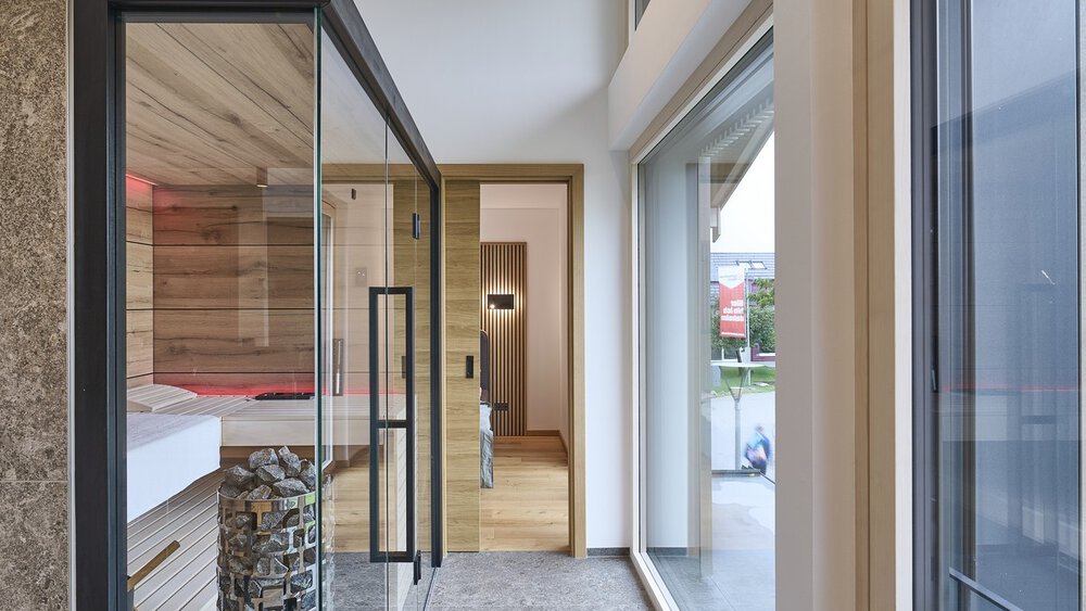 Eine moderne Sauna mit Glastüren, die zu  einem Schlafzimmer führen und hellem Tageslicht.