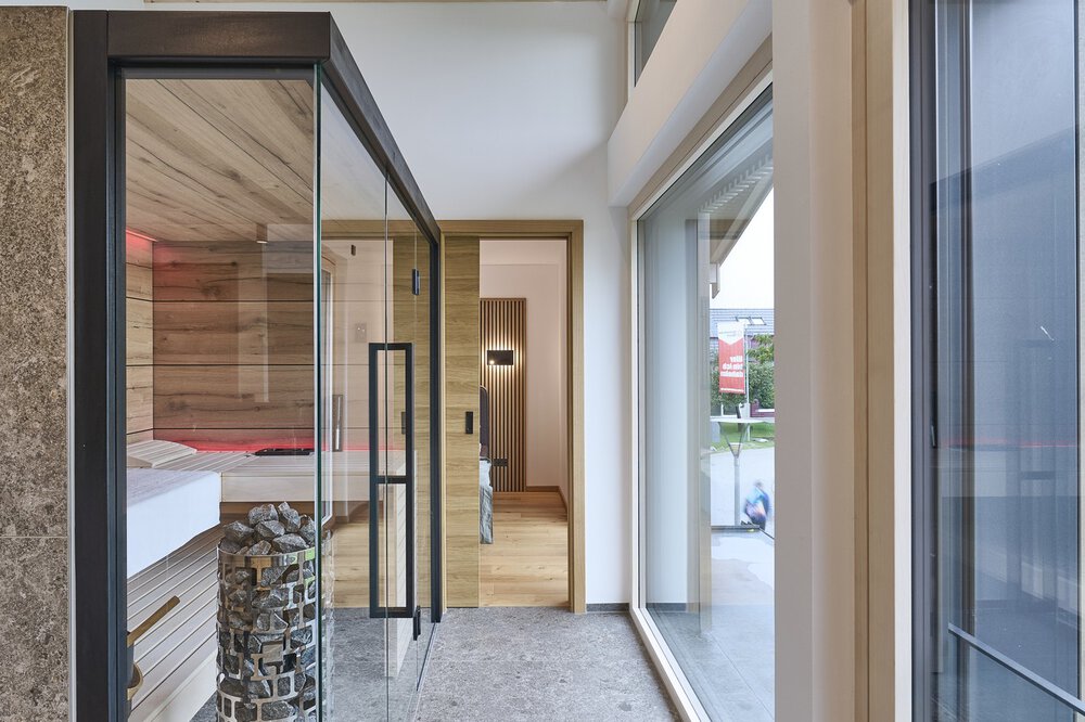 Eine moderne Sauna mit Glastüren, die zu  einem Schlafzimmer führen und hellem Tageslicht.