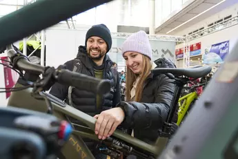 Two people stand at a bicycle stand and take a closer look at a bicycle.