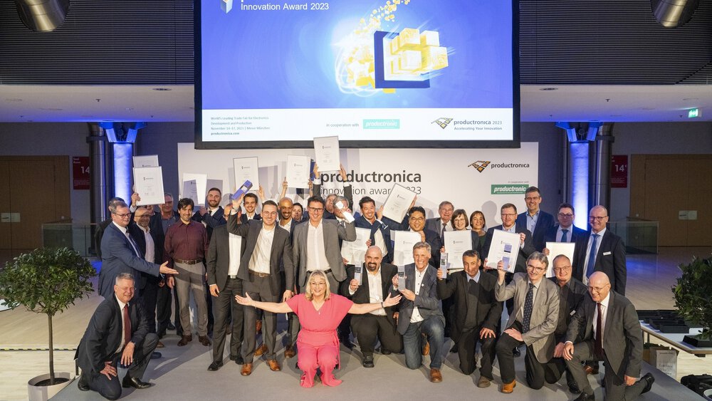 The numerous winners of the productronica Innovation Award 2023 pose together kneeling and standing with their prizes and certificates for a group photo.