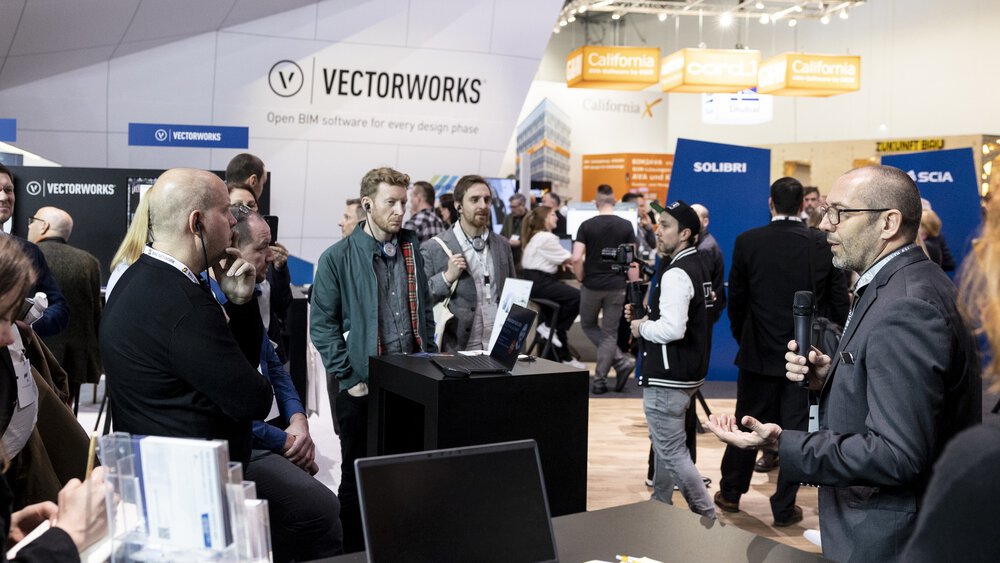 Menschen besuchen eine Präsentation an einem Vectorworks-Stand während einer belebten Industriemesse oder Konferenzveranstaltung.