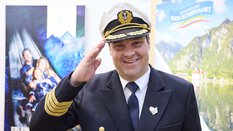 A ship captain at the Oberbayern booth waves cheerfully at the camera.