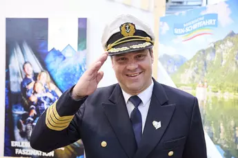 A ship captain at the Oberbayern booth waves cheerfully at the camera.