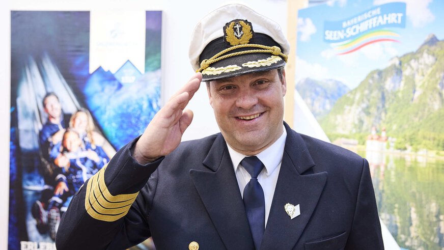A ship captain at the Oberbayern booth waves cheerfully at the camera.