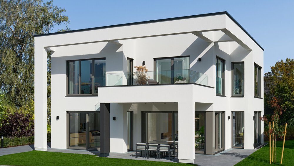 Modernes zweistöckiges weißes Haus mit großen Fenstern, einem Balkon und umgeben von Grün.