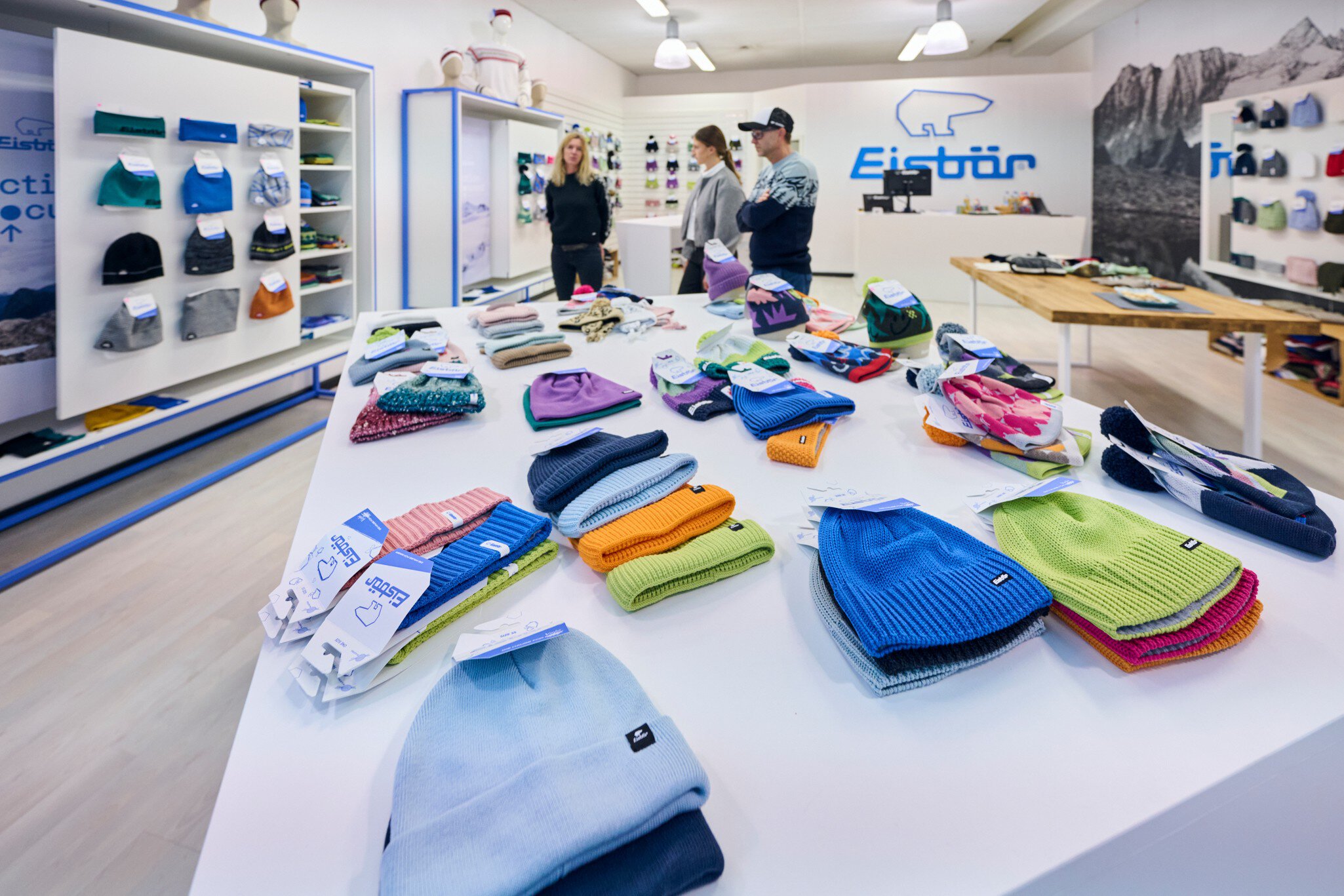 Ein Ausstellungsbereich für Wintersportbekleidung. Auf Tischen liegen und an Displays hängen bunte Mützen und Stirnbänder der Marke „Eisbär“.