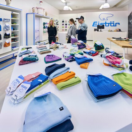 Ein Ausstellungsbereich für Wintersportbekleidung. Auf Tischen liegen und an Displays hängen bunte Mützen und Stirnbänder der Marke „Eisbär“.