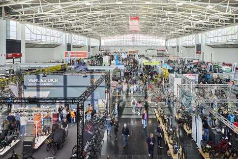 Eine Messehalle von oben mit zahlreichen Ausstellungsbereichen und vielen Besuchern, die sich unterschiedliche Fahrräder ansehen.