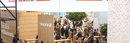 View of a large joint stand of REWE, PENNY and toom. Numerous visitors stand together in small groups or walk through the aisles.