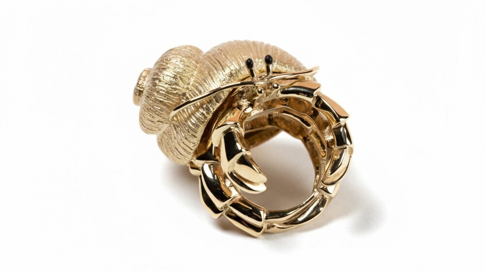 A close-up view of a gold ring that resembles a crab with a gold shell, antennae, and black beady eyes.