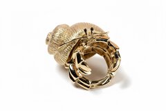 A close-up view of a gold ring that resembles a crab with a gold shell, antennae, and black beady eyes.