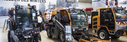 Three road sweepers on display at an exhibition stand. In front of it is a stand with information brochures.