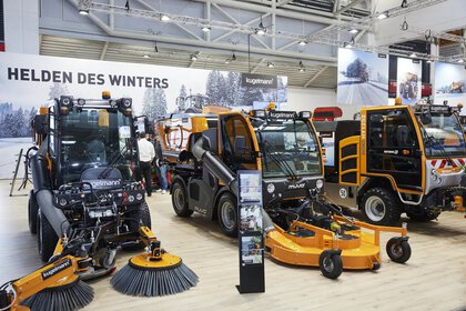 Three road sweepers on display at an exhibition stand. In front of it is a stand with information brochures.