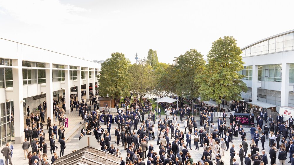 Numerous people standing and talking in an outdoor area of an exhibition center.