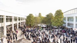 Numerous people standing and talking in an outdoor area of an exhibition center.