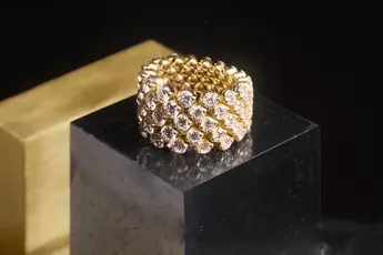 Ein mit mehreren Reihen Diamanten besetzter Goldring sitzt auf einem schwarzen Sockel vor einem dunklen Hintergrund.