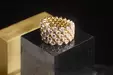 A gold ring set with several rows of diamonds sits on a black base against a dark background.