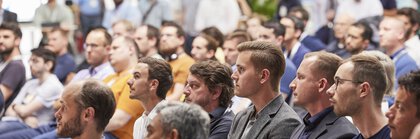 Aufmerksames Publikum in einer Messehalle.