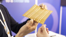 Two people holding a flexible electronic circuit board with a blurred background.