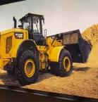 A yellow CAT wheel loader with front shovel operates between piles of earth and building materials.