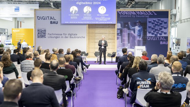 A speaker addresses a seated audience on the 