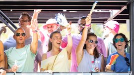 A group of people smiling, waving, and cheering at an outdoor event in bright sunshine.