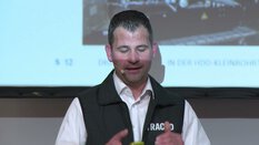 Ein Mann in Weste und Hemd erklärt vor einem Bildschirm eine technische Präsentation.