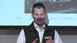 A man in a waistcoat and shirt explains a technical presentation in front of a screen.