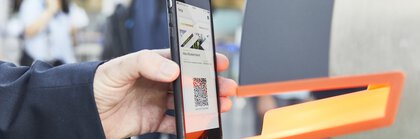 Person scanning a QR code on their smartphone at a ticket barrier.