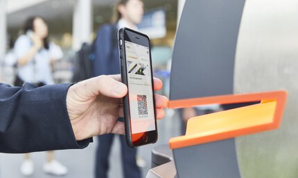 Person scanning a QR code on their smartphone at a ticket barrier.