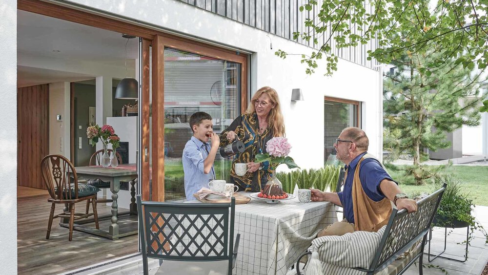 Ein älteres Paar sitzt zusammen mit einem kleinen Jungen bei Kaffee und Kuchen auf einer Terrasse.