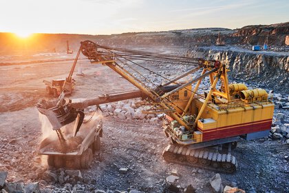A huge mining excavator loads stones into a dump truck at sunset.