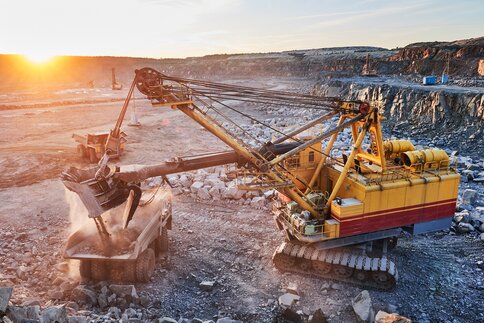 A huge mining excavator loads stones into a dump truck at sunset.