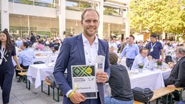 A winner of the 2025 Innovation Award holds his certificate in his hand, with people sitting on beer benches in the background.