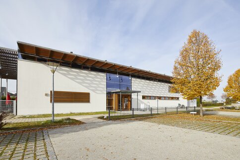 Modernes Gebäude mit großem Glaseingang, Holzakzenten und der Aufschrift 