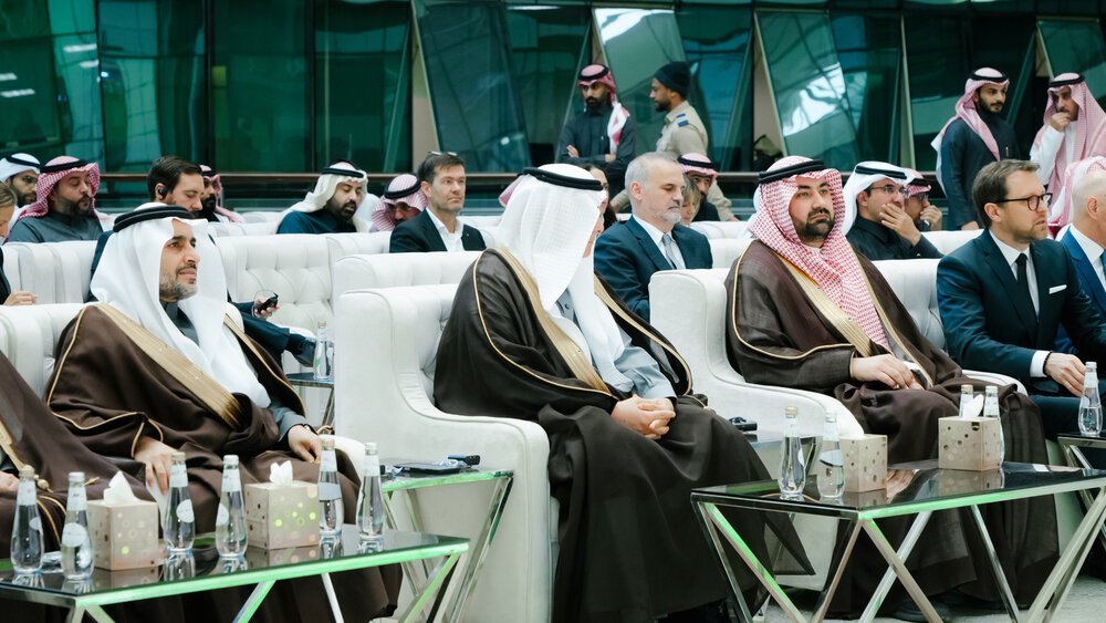 People sit at an event, others stand in the background in a modern ambience.