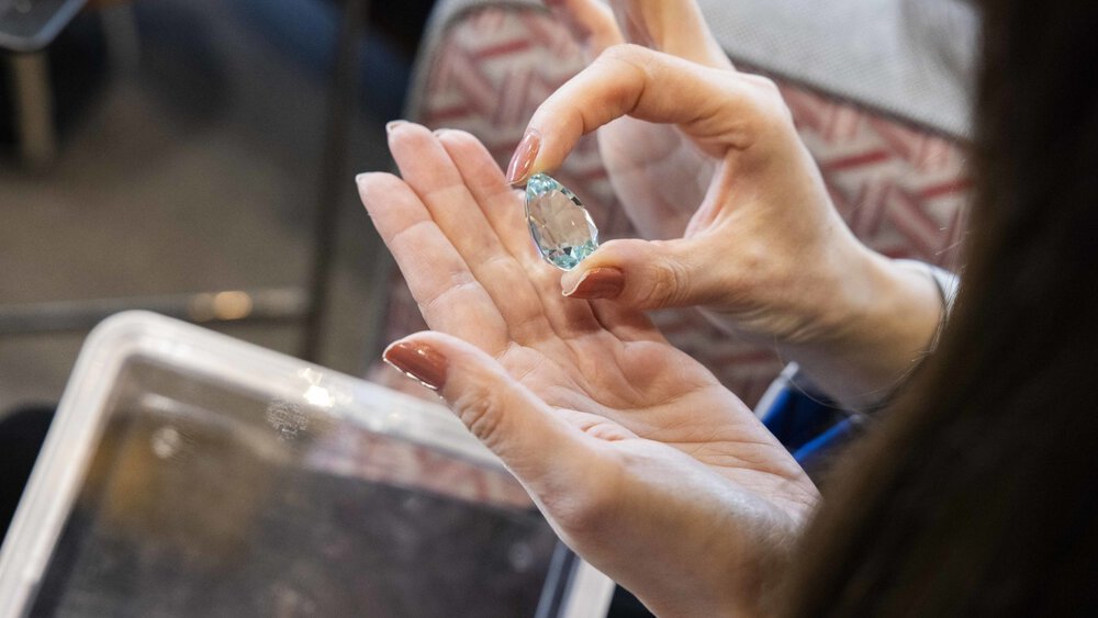 Hands holding a large, round, clear gemstone over a small container.