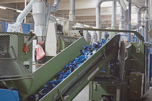 Ein Förderband transportiert blaue Textilschnippsel.
