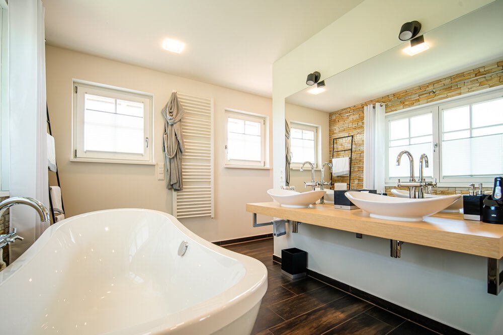 Modernes Badezimmer mit freistehender weißer Badewanne, Doppelwaschbecken, großem Spiegel und Holzakzenten.