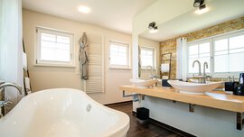 Modernes Badezimmer mit freistehender weißer Badewanne, Doppelwaschbecken, großem Spiegel und Holzakzenten.