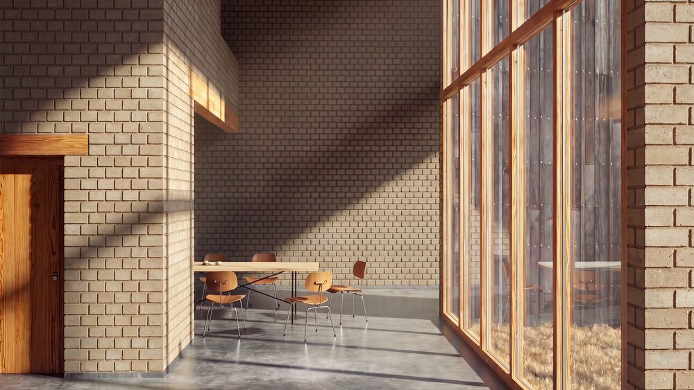 Sunlit interior with brick walls, large wood-framed windows, a simple table and four chairs on a concrete floor.