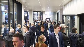 Visitors to the BAU trade fair stream through a spacious, brightly lit corridor. Some stand together in groups and chat.