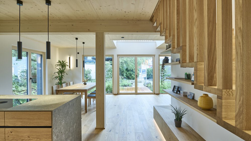 Moderne Küche mit Holzschränken, Hängelampen und großen Fenstern mit Blick ins Grüne.