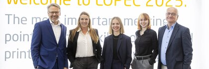 Drei Frauen und zwei Männer in Anzügen stehen vor einer Fotowand der LOPEC 2025 und lächeln gemeinsam für ein Gruppenbild.