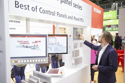 Person interacting with control panels and panel PCs with a touchscreen at a technology exhibition stand.