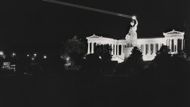 Schwarzweißfoto der Bavaria Statue bei Nacht, der Loorbeerkranz in der Hand der Statue wird von einem Laser angestrahlt und ist hell erleuchtet.